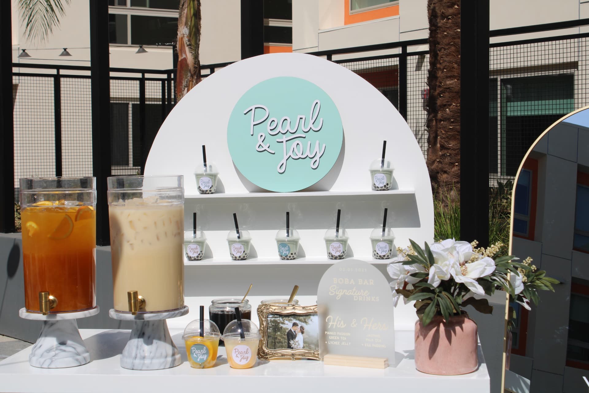 Elegant quinceañera boba bar station with bubble tea dispensers, fresh fruit toppings, and pink and sage themed cups at a Southern California celebration
